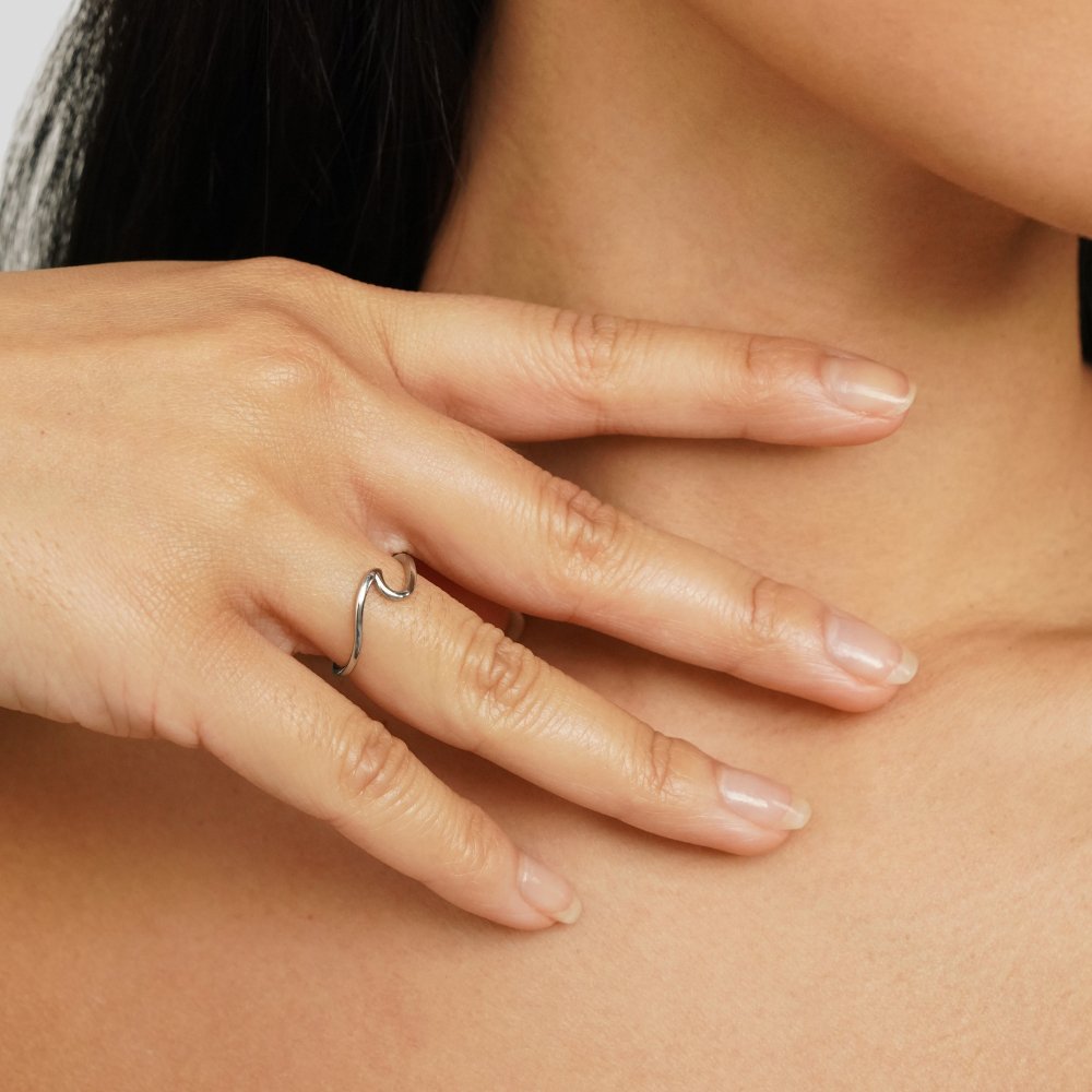 Imari Silver Wave Ring, worn on a hand against a bare neck, silver wave band