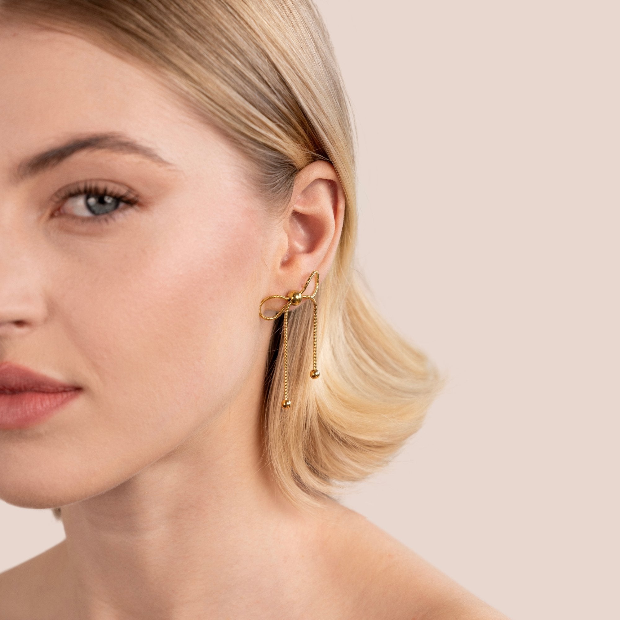 Katie Bow Earrings, worn on an ear, gold bow with two dangling chains