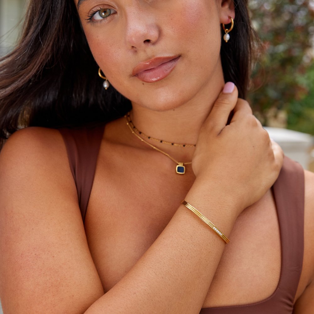 Kim Crystal bangle, worn on a wrist with gold layered necklaces and hoop earrings