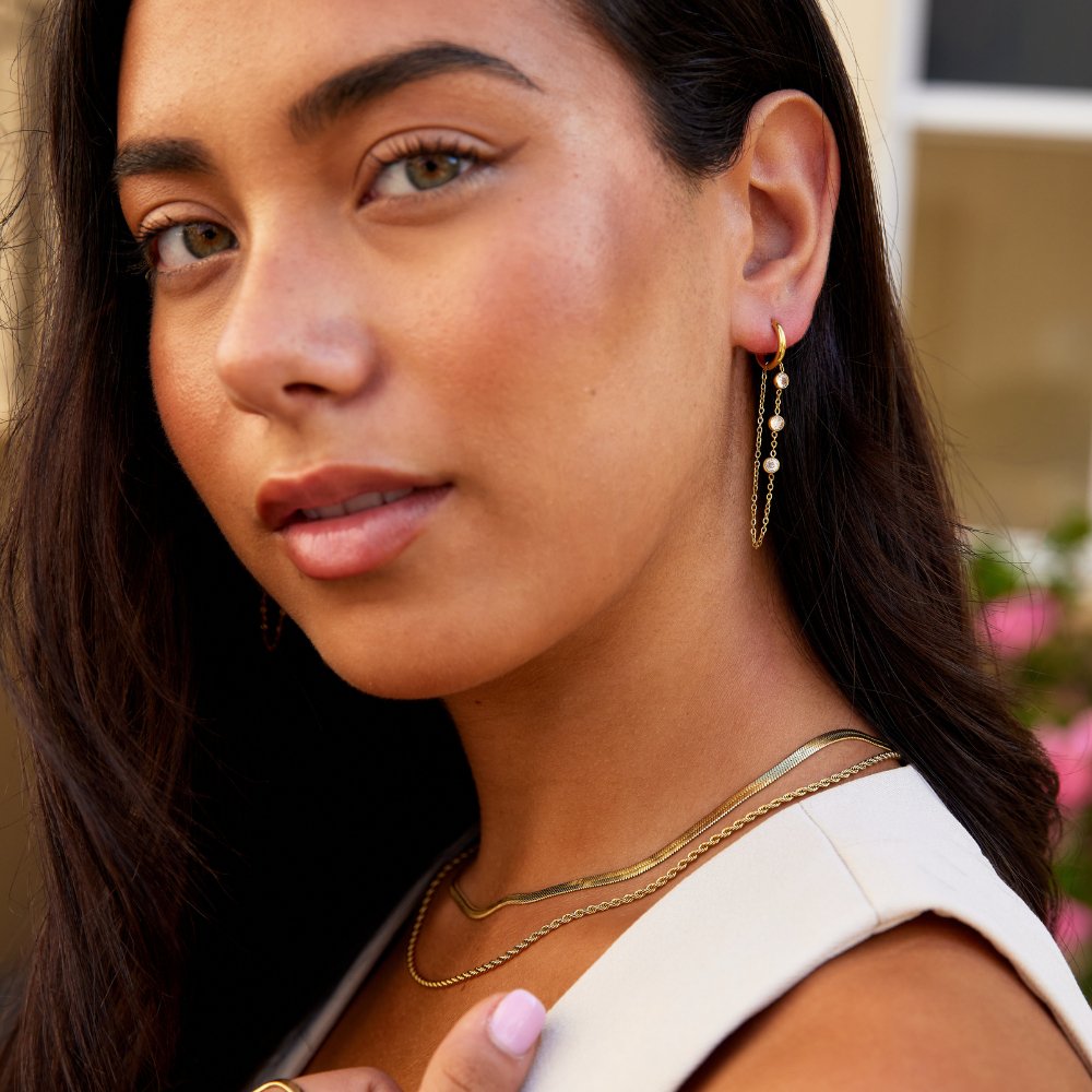 Kira Crystal Drop Hoop Earrings, worn on a woman with layered gold necklaces, close-up