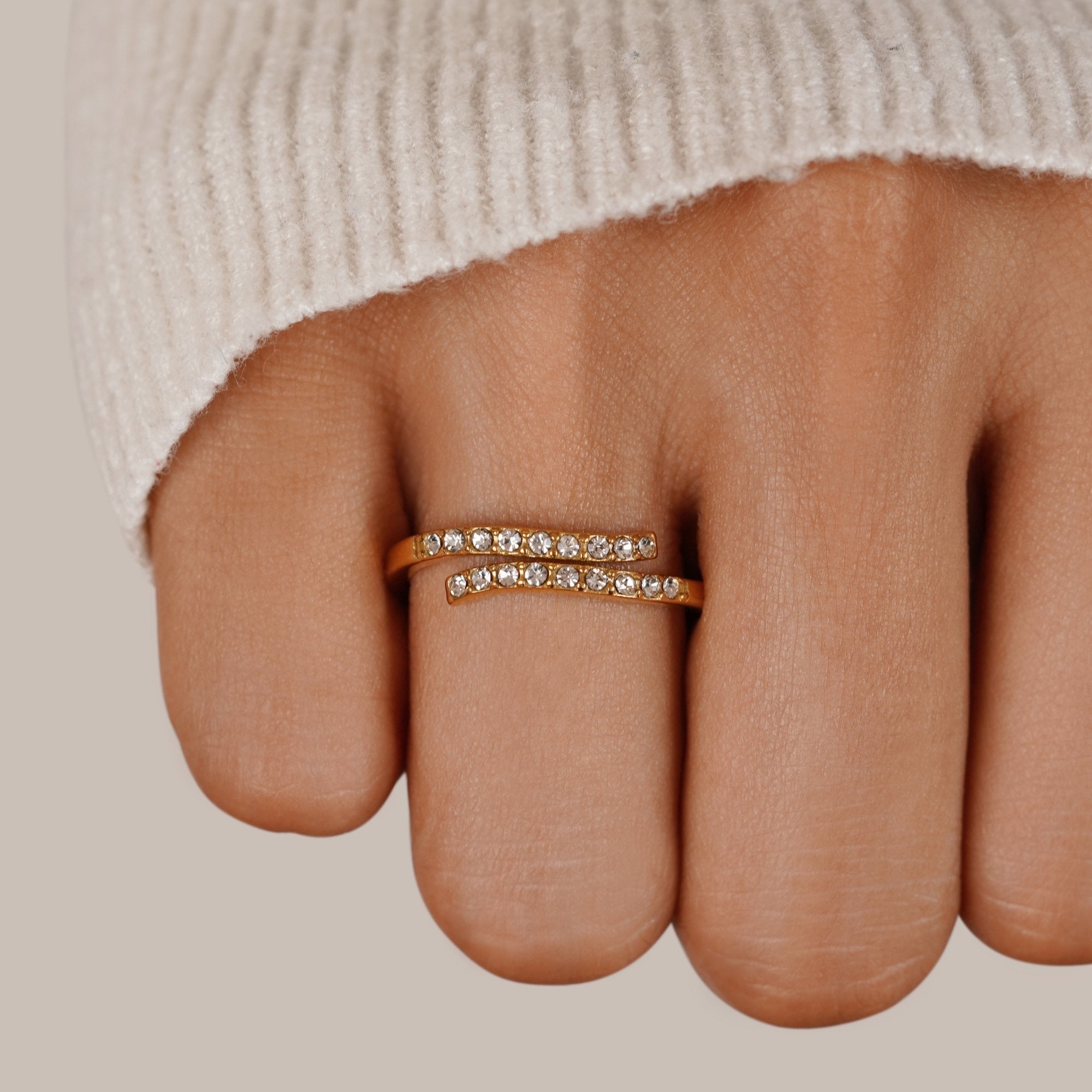 Layered Gold & Crystal Wrap Ring, worn on a finger in a cream knit sleeve, gold with crystals