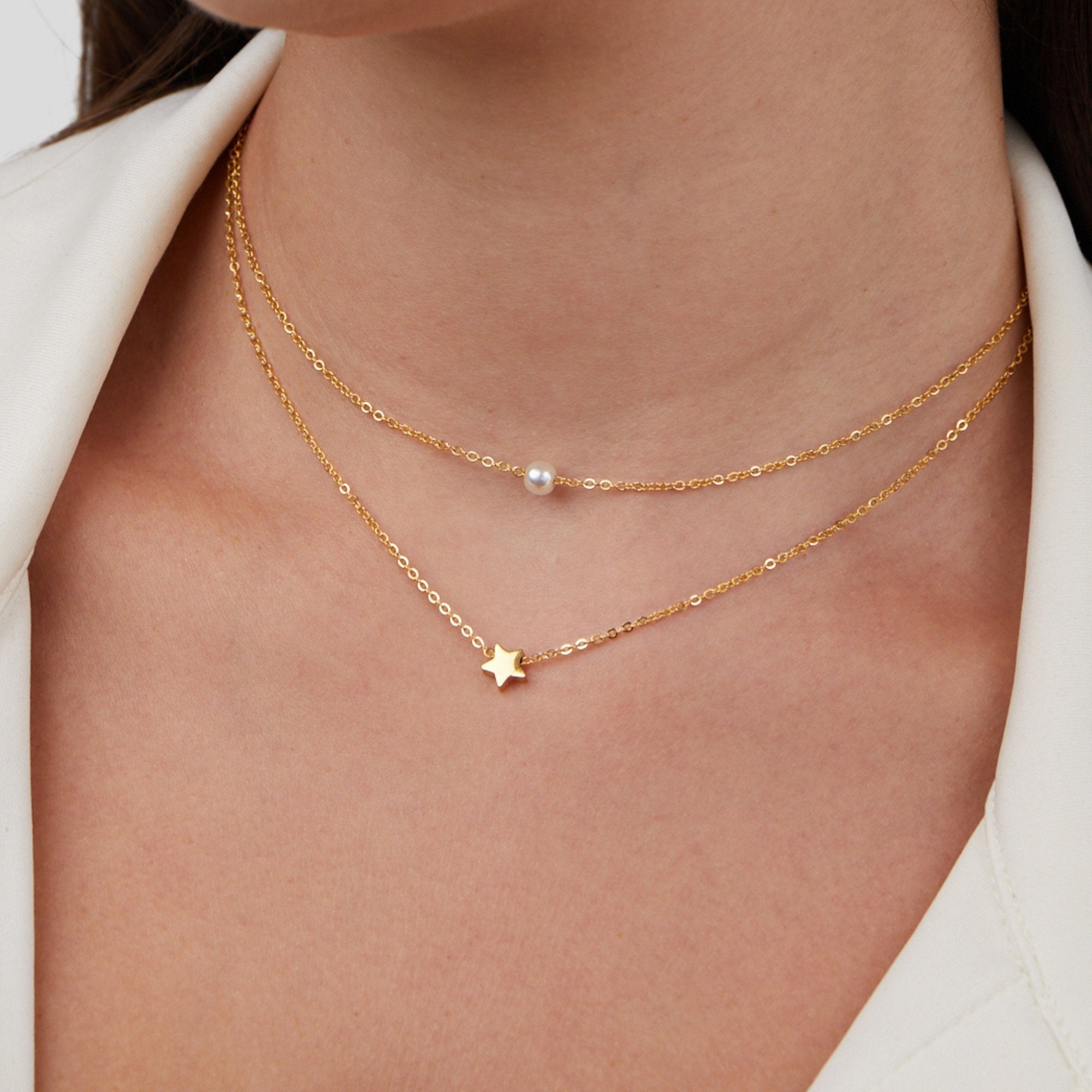 Layered Gold Star & Pearl Necklace, worn on a neck with a white collar, close-up of two gold chains