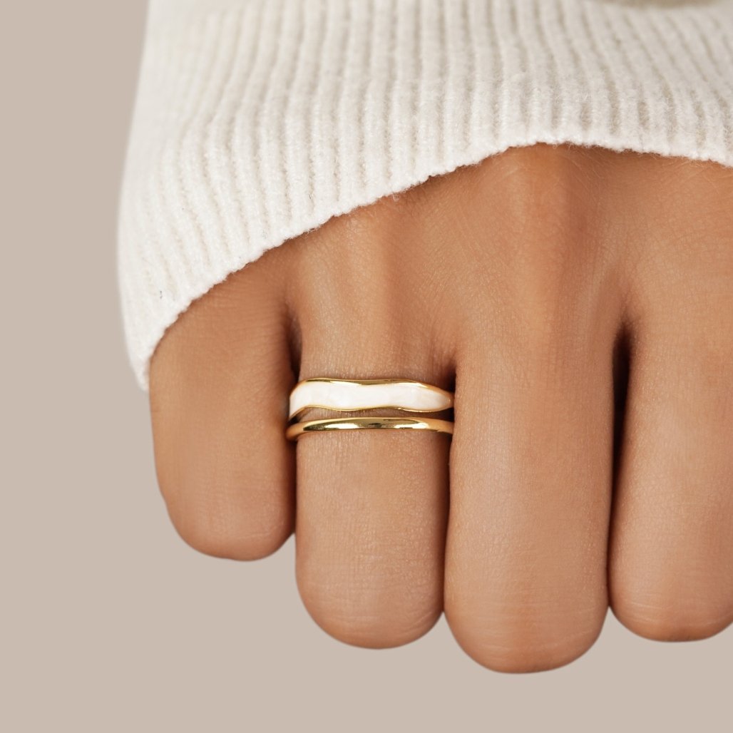 Layered Sahara Gold Ring, worn on a finger in a cream knit sleeve, gold with white enamel