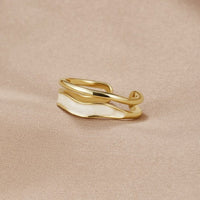 Layered Sahara Gold Ring, lying on beige fabric, gold band with white enamel wave