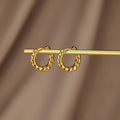 Layla Gold Twist Earrings, pair of twisted gold hoops hanging on a gold rod against brown fabric