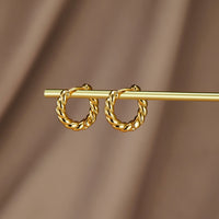 Layla Gold Twist Earrings, pair of twisted gold hoops hanging on a gold rod against brown fabric