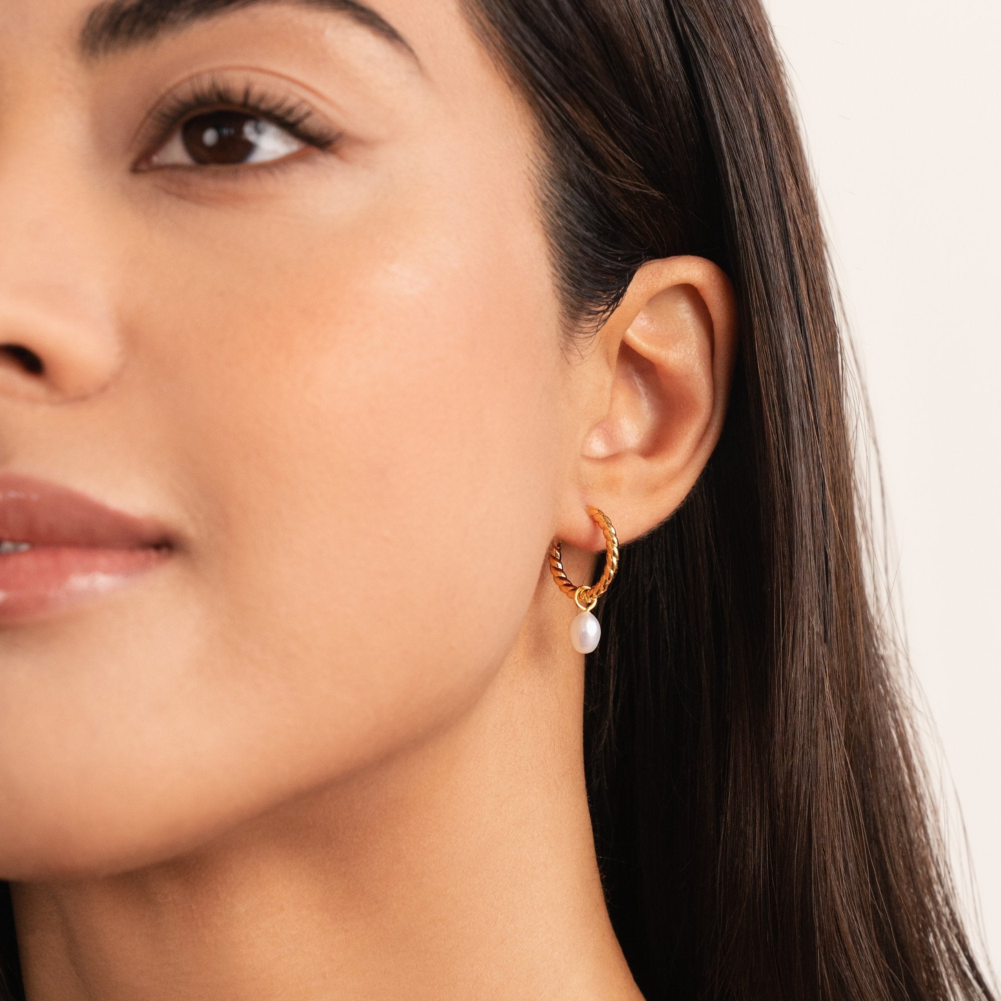 Layla Pearl Twist Earrings, worn on an ear, gold twisted hoop with a hanging pearl