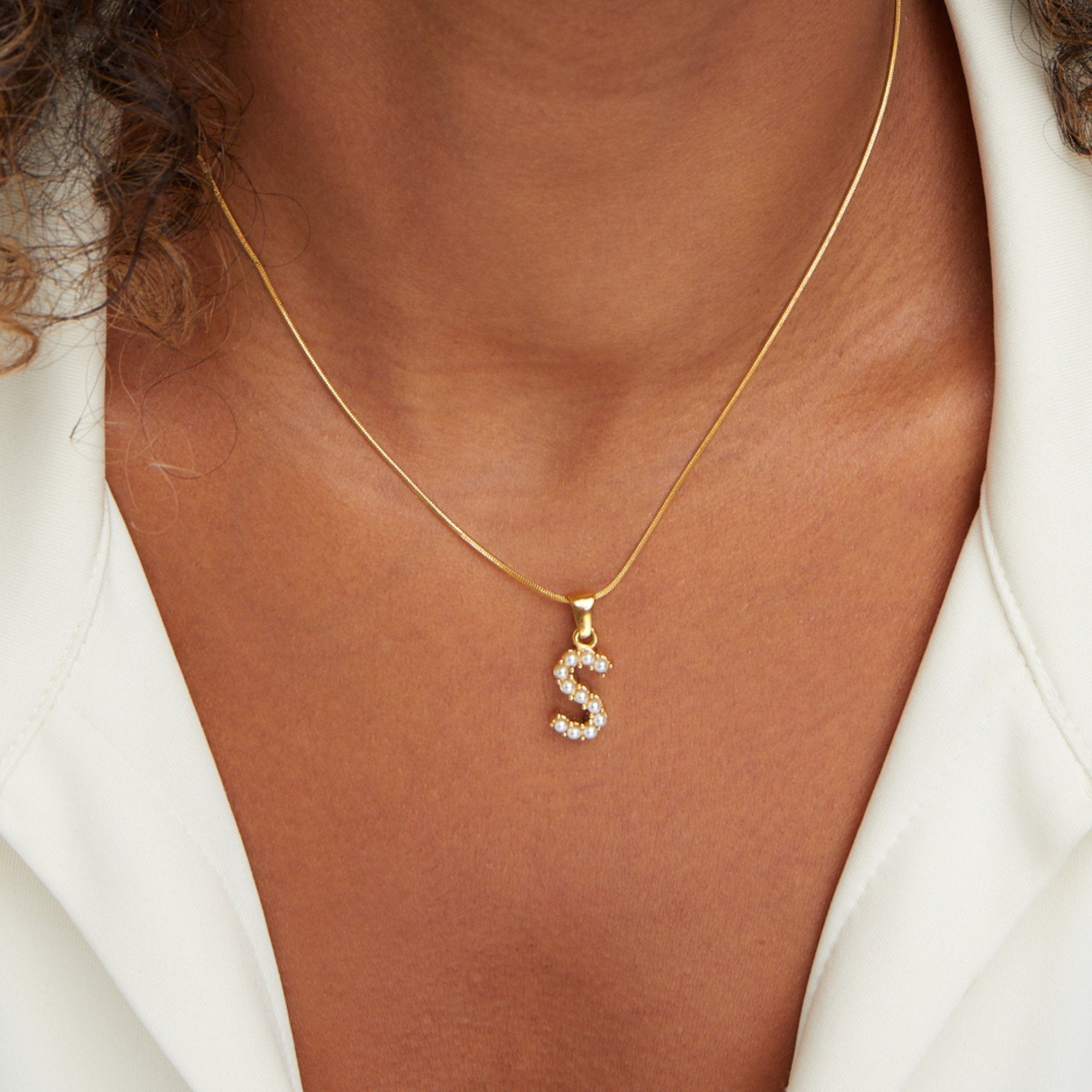 Letter Pearl Charm Necklace, worn on a neck with a white open-collar shirt, gold S pendant
