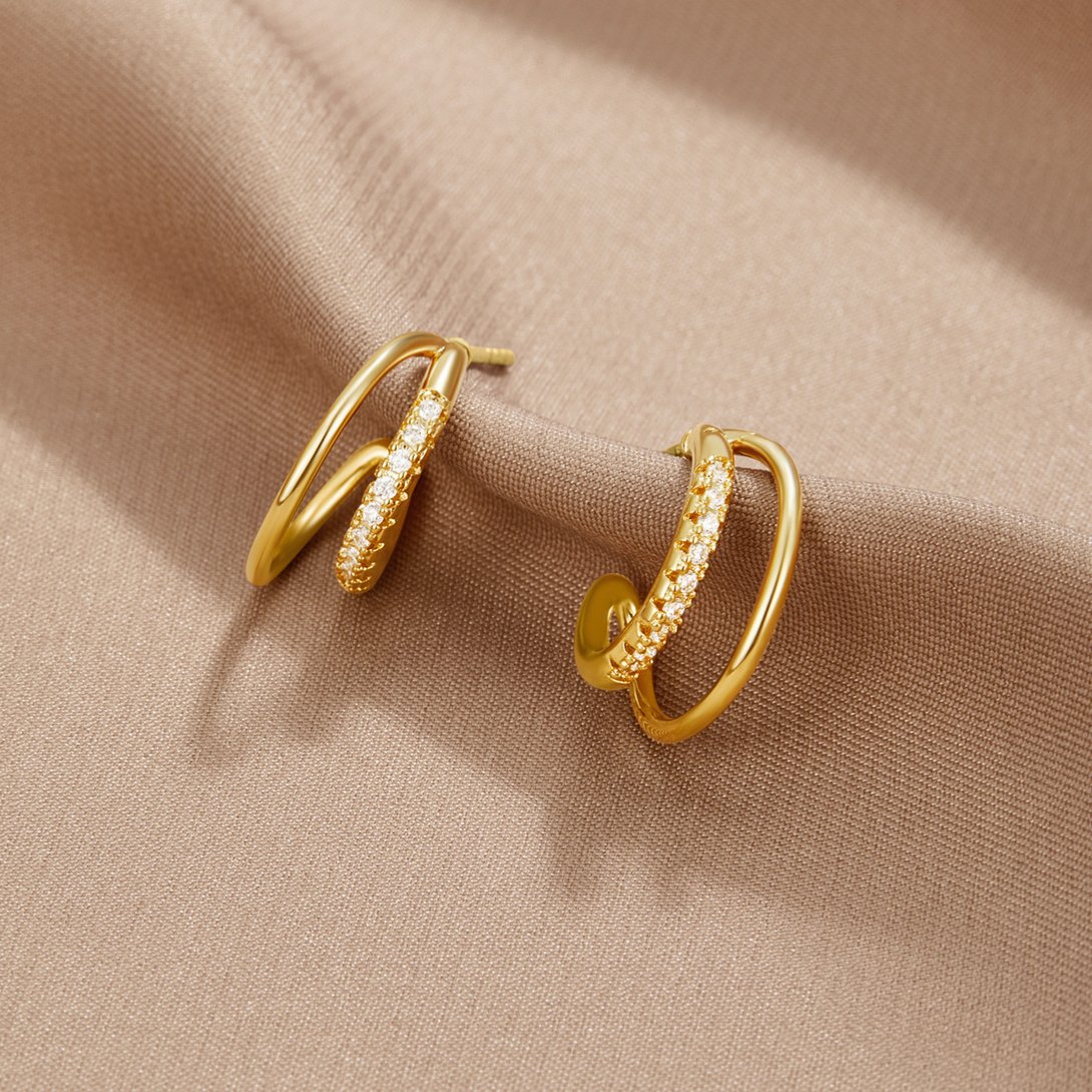 Leyla Crystal Double Hoop Earrings, a pair of gold earrings on a beige fabric, one plain and
