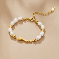 Lovina Pearl Bracelet, laid flat on beige fabric, white pearls and gold beads, wavy gold bar