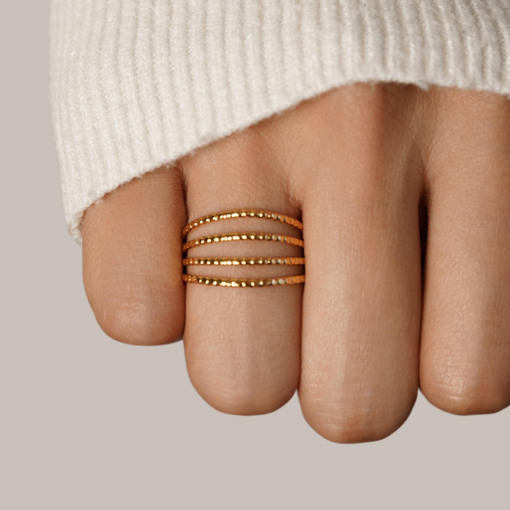Madison 18K Layered Ring, worn on a finger with a cream knit sleeve behind, four textured gold bands