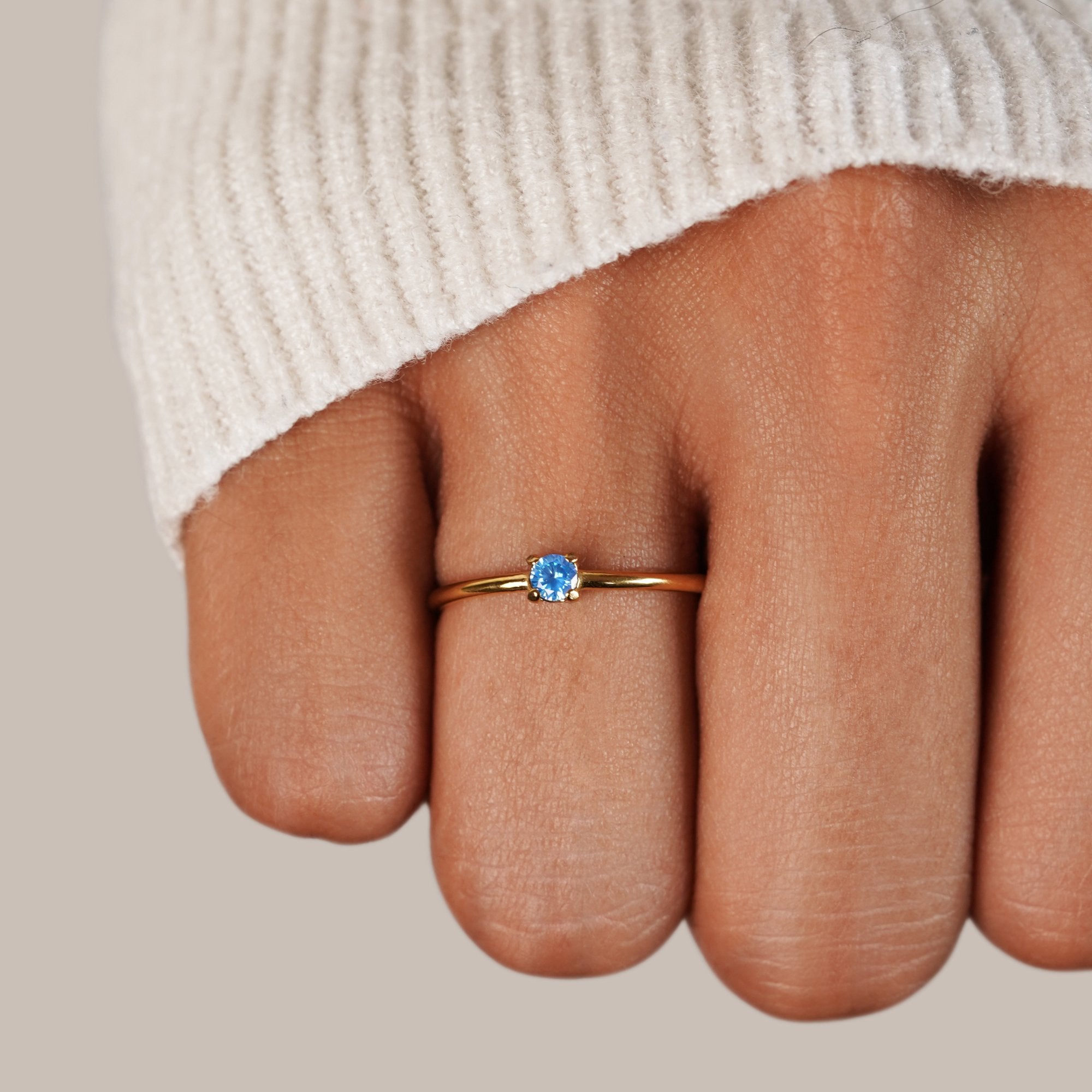 March Birthstone 18K Gold Ring, worn on a hand in a cream knit sleeve, blue stone