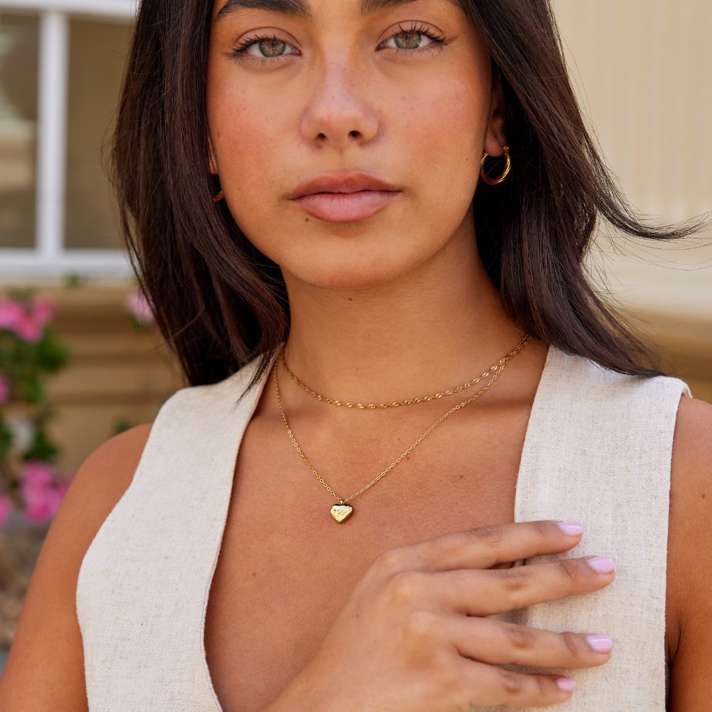 Marina Love Gold Necklace, worn layered at the neck with a gold heart pendant, hand resting on chest