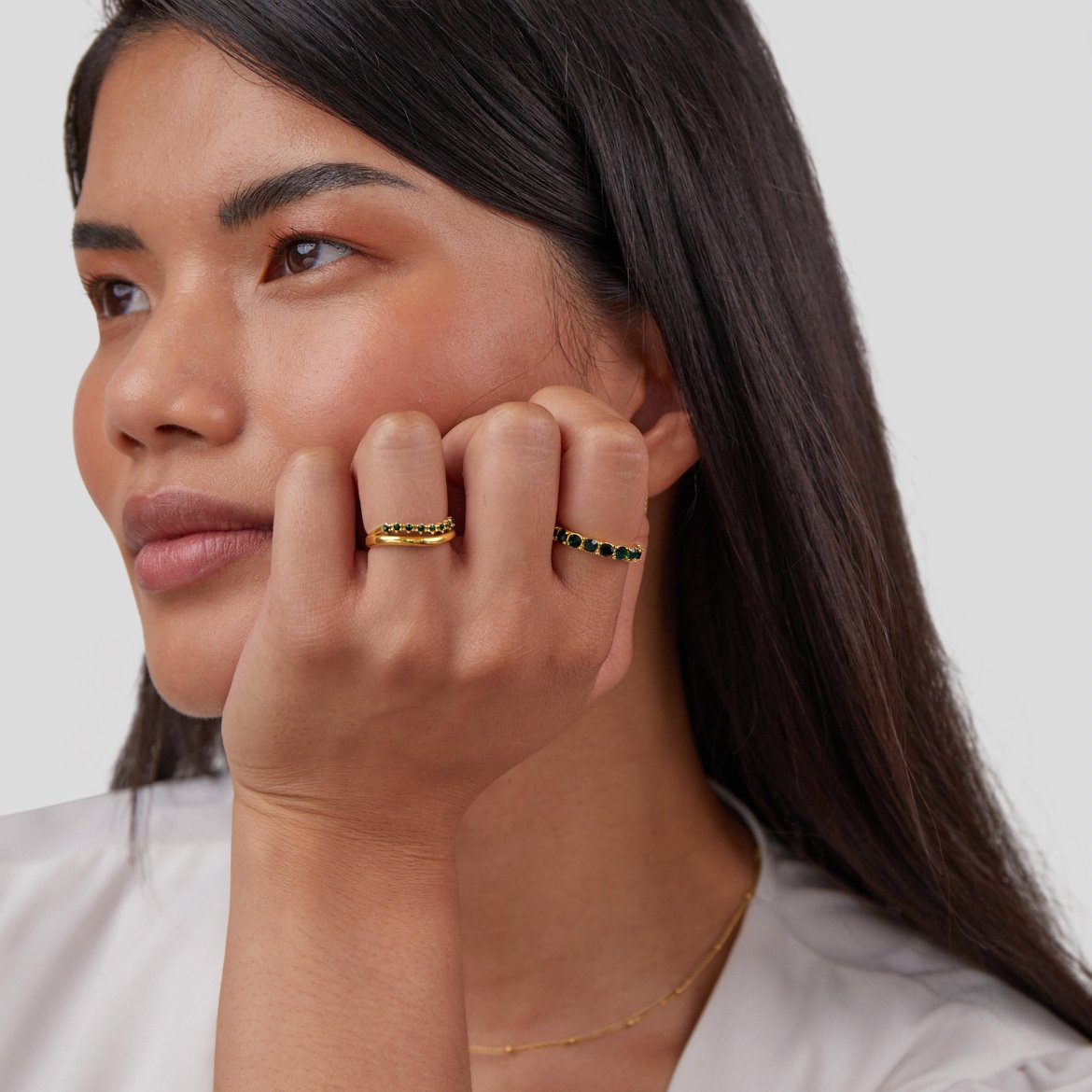 Marissa Emerald Green Layered Ring, worn on a hand resting against a cheek, two gold rings visible