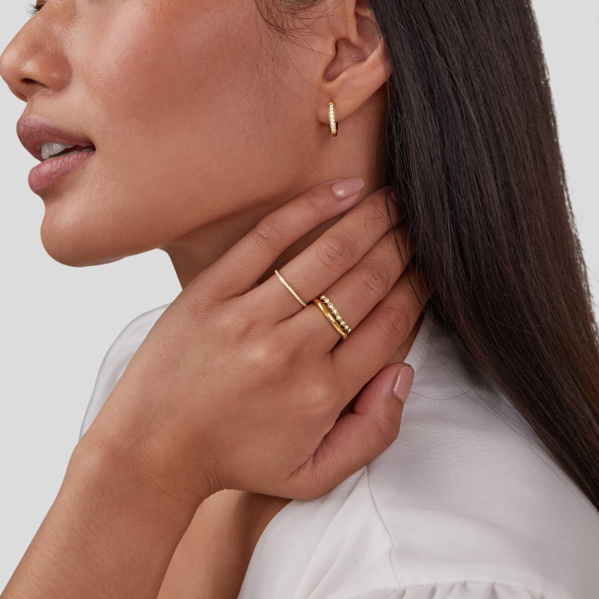 Marissa White Crystal Layered Ring, worn on a hand at the neck with a gold hoop earring