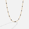 Mila Black Bead Necklace, gold chain necklace with black enamel beads, laid on a light background