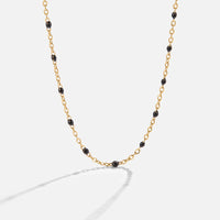 Mila Black Bead Necklace, gold chain necklace with black enamel beads, laid on a light background