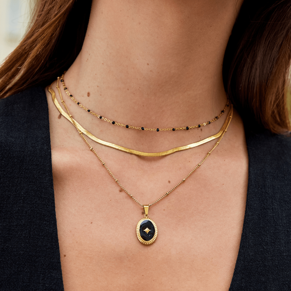 Mila Black Bead Necklace, worn layered at a neck, with a dark oval pendant with gold star