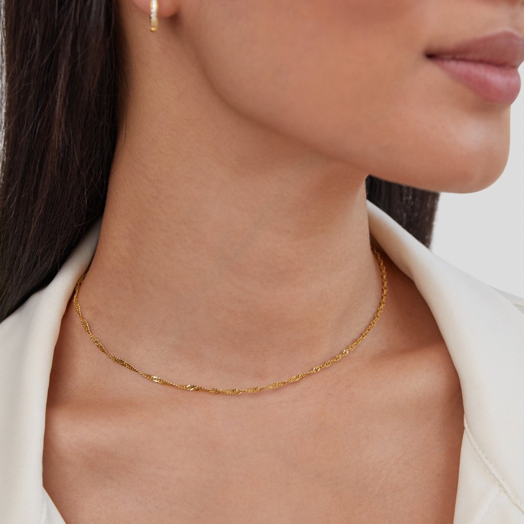 Mila Twist Gold Chain Necklace, worn on a neck with a white jacket and gold hoop earring