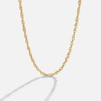 Mila Twist Gold Chain Necklace, gold twisted chain lying in a curve on a pale background