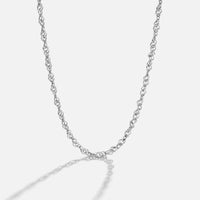 Mila Twist Silver Chain Necklace, laid out in a curving loop on white, with a shadow cast below