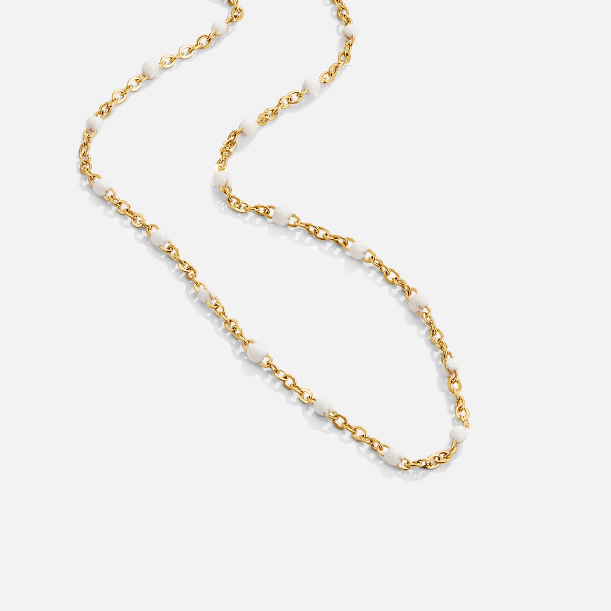 Mila White Bead Necklace, gold chain necklace with white beads, laid out in a loose curve on white