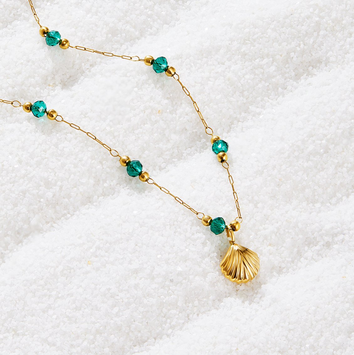 Nerissa Gold Shell & Green Bead Necklace, laid on white sand with a gold shell pendant and