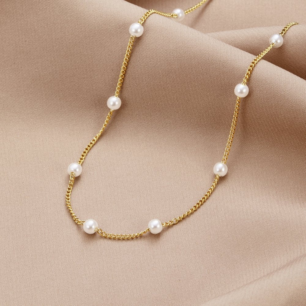 Nura Pearl 18K Gold Necklace, laid flat on draped beige satin, gold chain with white pearls