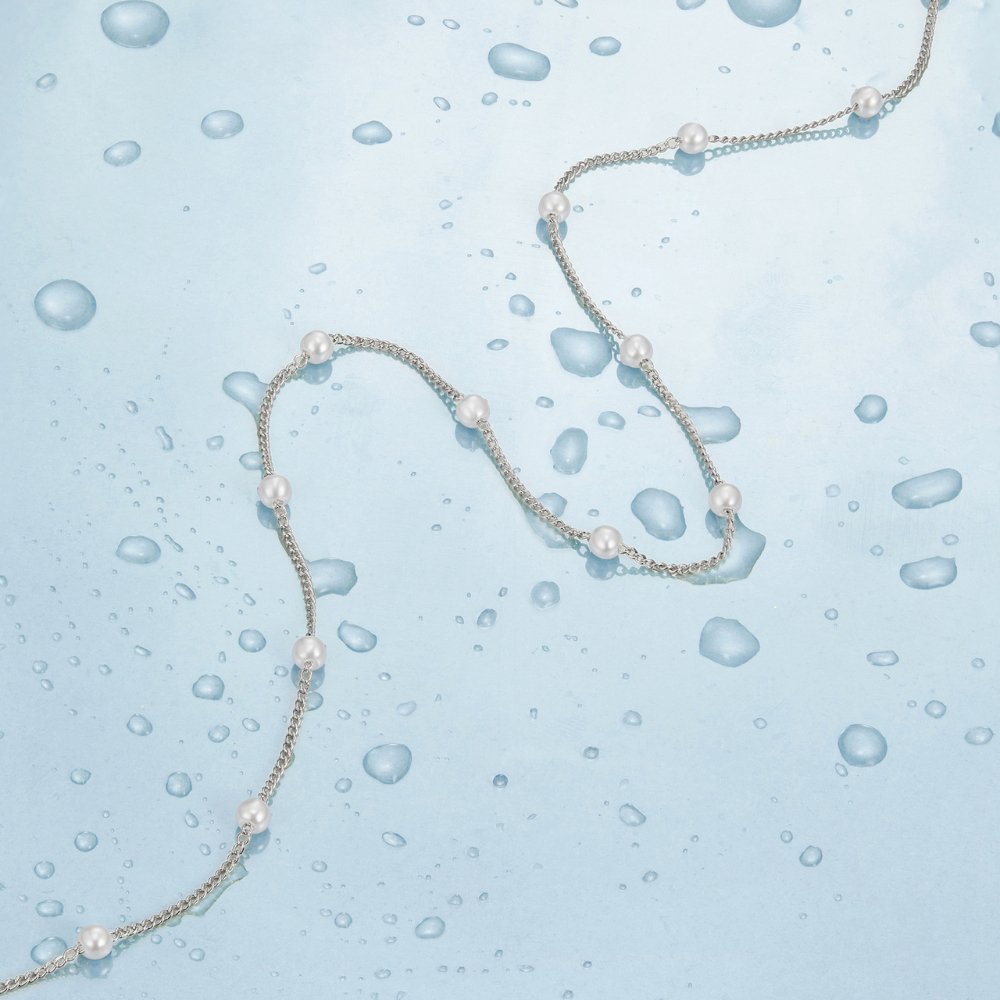 Nura Pearl Silver Necklace, chain necklace with white pearls laid across wet blue surface