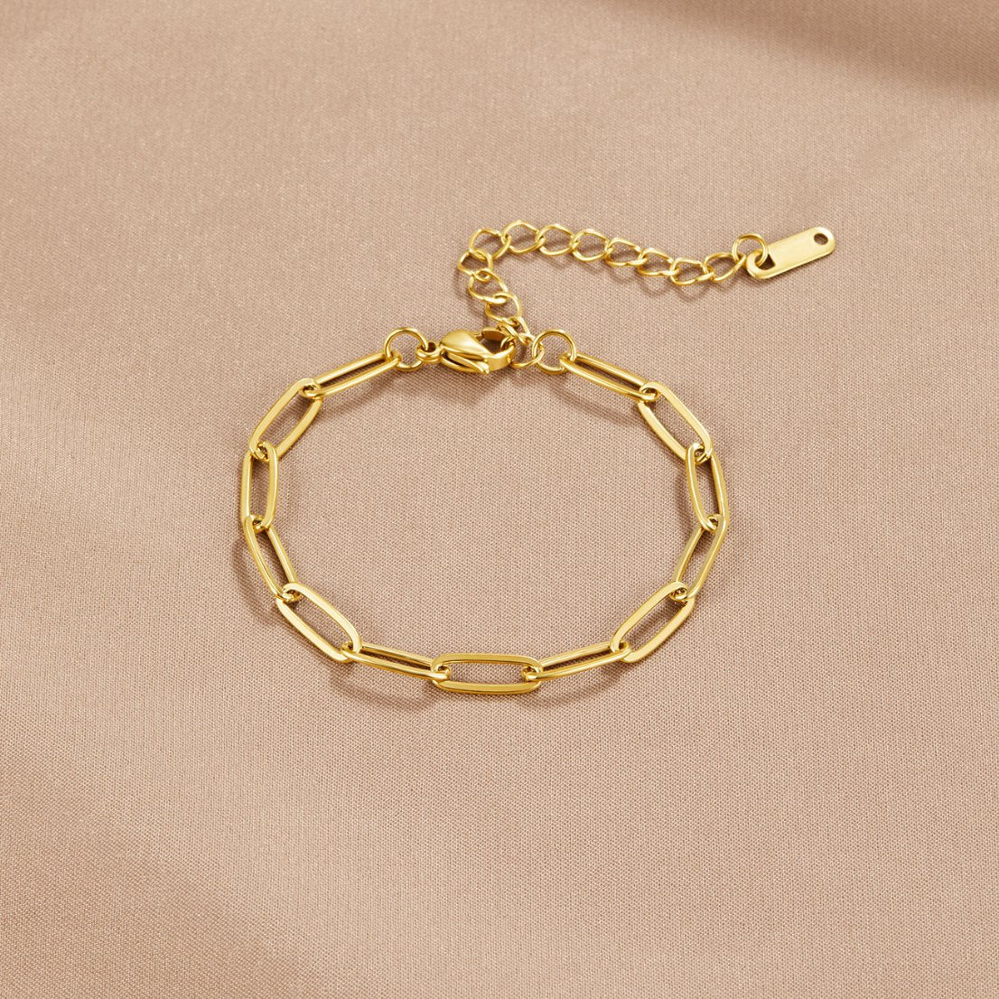 Paperclip Gold Bracelet, laid flat on a beige satin cloth, clasp and extender visible