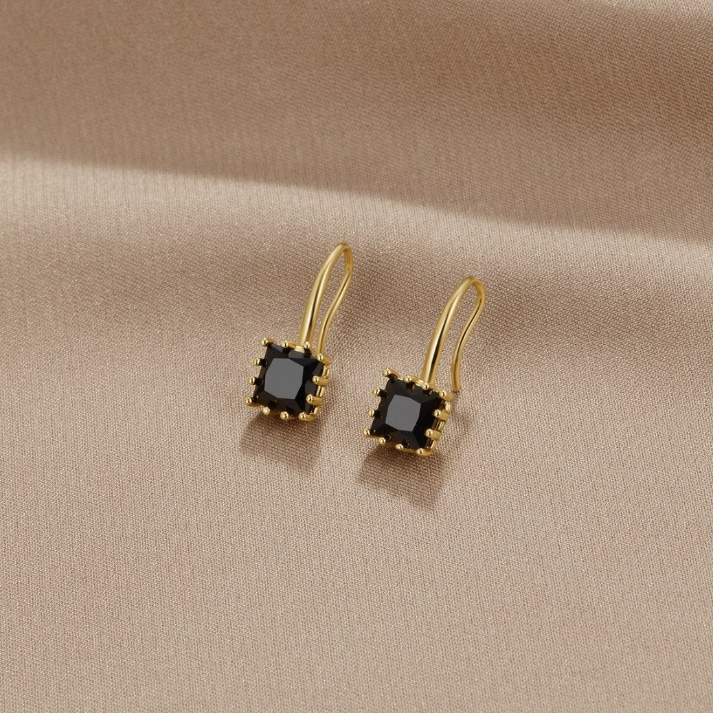 Piper Black Crystal Drop Earrings, a pair of gold earrings with square black stones on beige