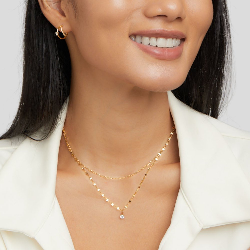 Piya Crystal Layered Necklace, worn on a smiling model with a gold hoop earring and white jacket