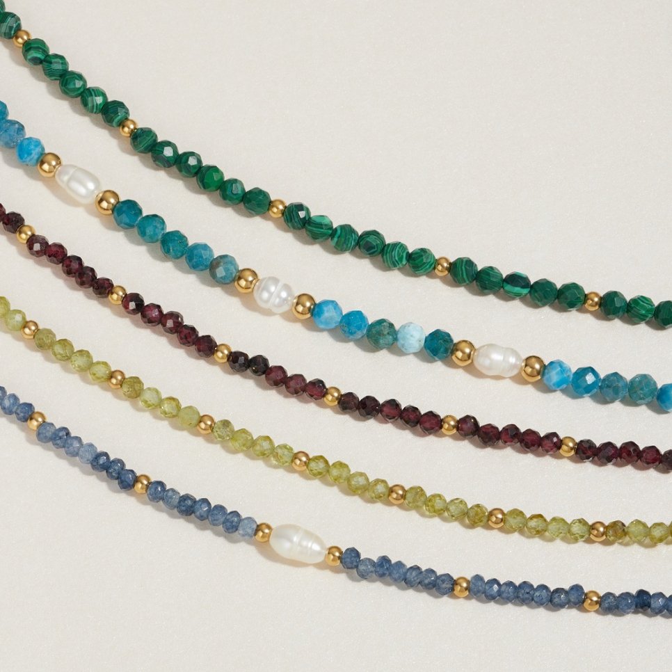 Red Garnet Bead Bracelet, five beaded strands laid side by side on pale stone, gold spacers
