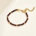 Red Garnet Bead Bracelet, bracelet laid flat on cream, dark red faceted beads with gold spacers