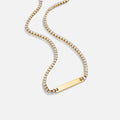 Rina Crystal Necklace, laid out on white, gold bar pendant on a crystal chain