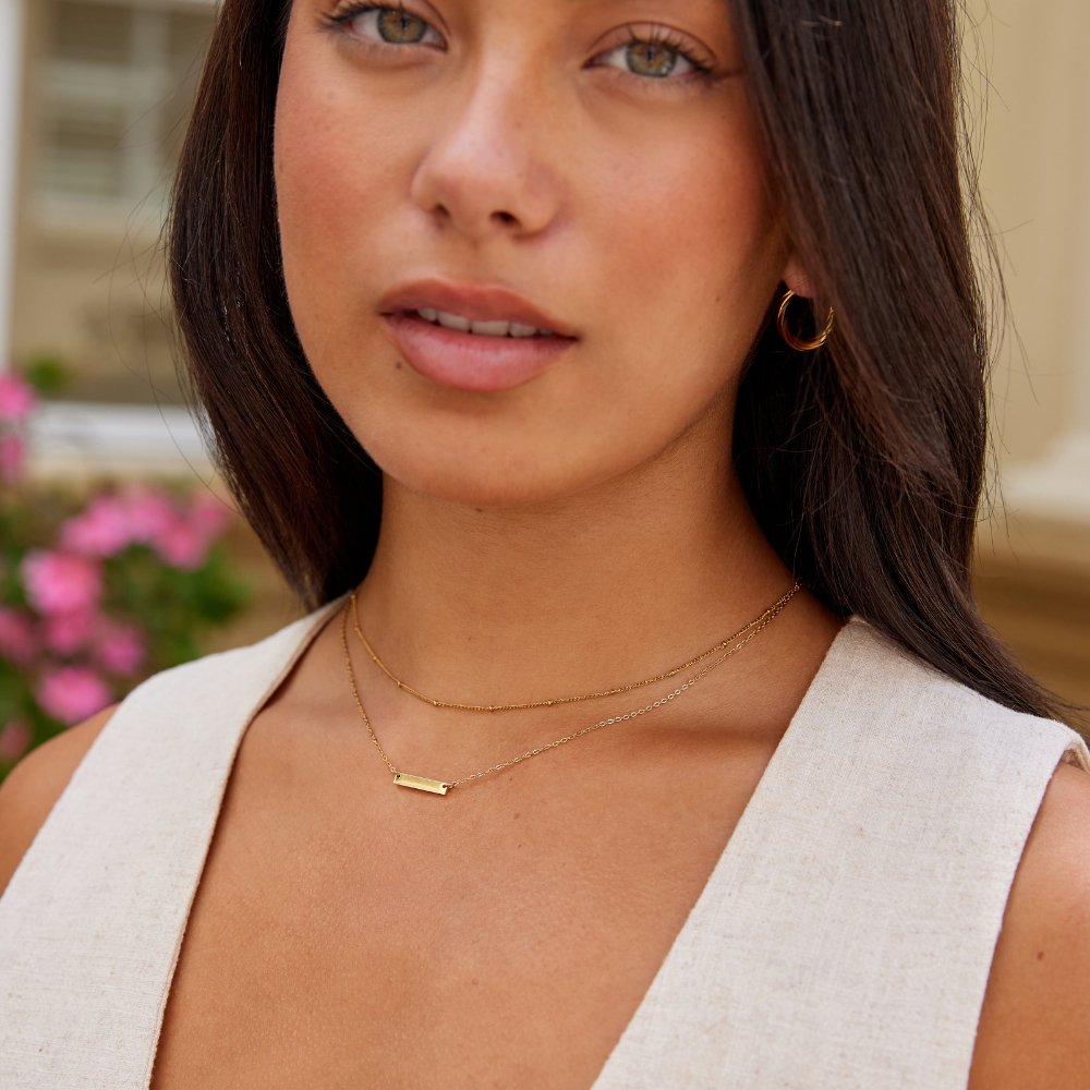 Rina Gold Bar Necklace, worn layered at the neckline with a gold bar pendant on a model