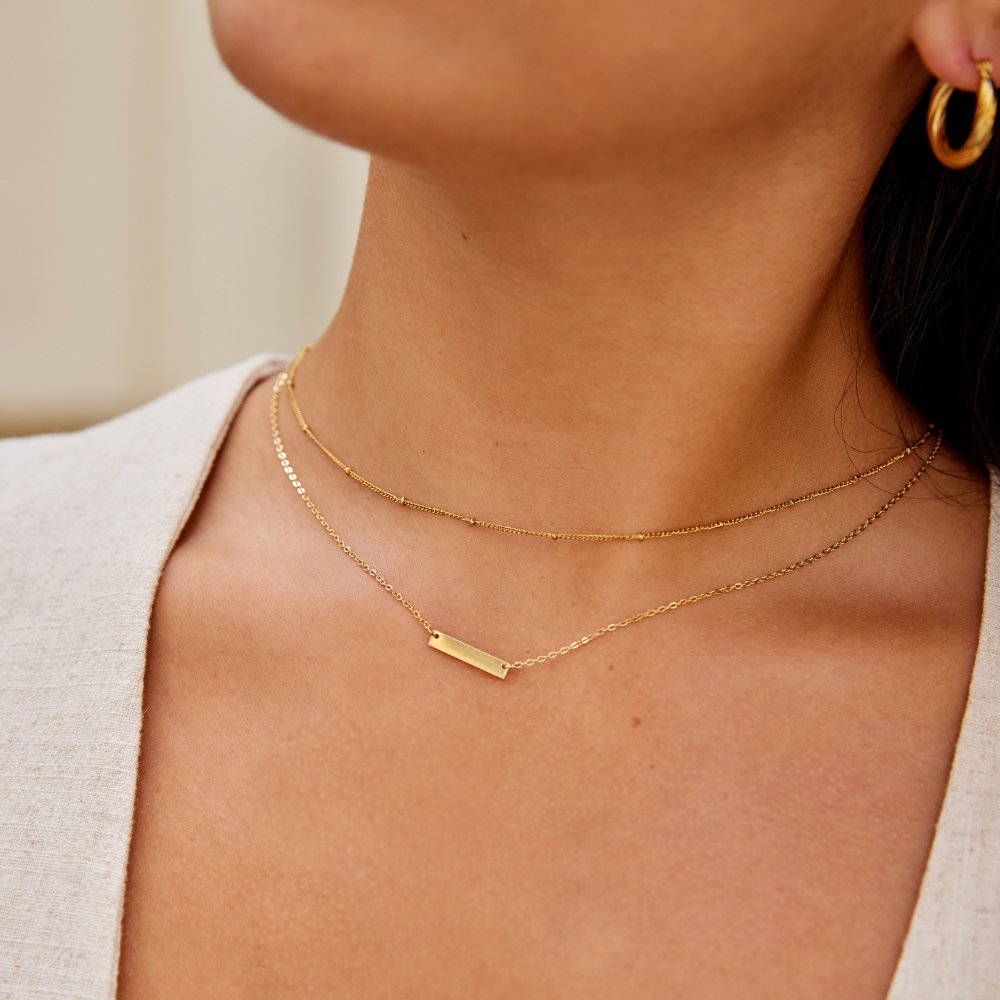 Rina Gold Bar Necklace, worn at the neck with a beaded layered chain and gold hoop earring