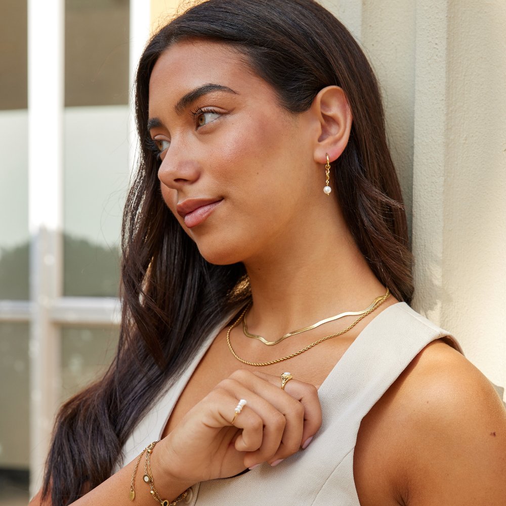 Rini Pearl Tassel Earrings, worn on a model with gold necklaces, bracelets and a pearl ring