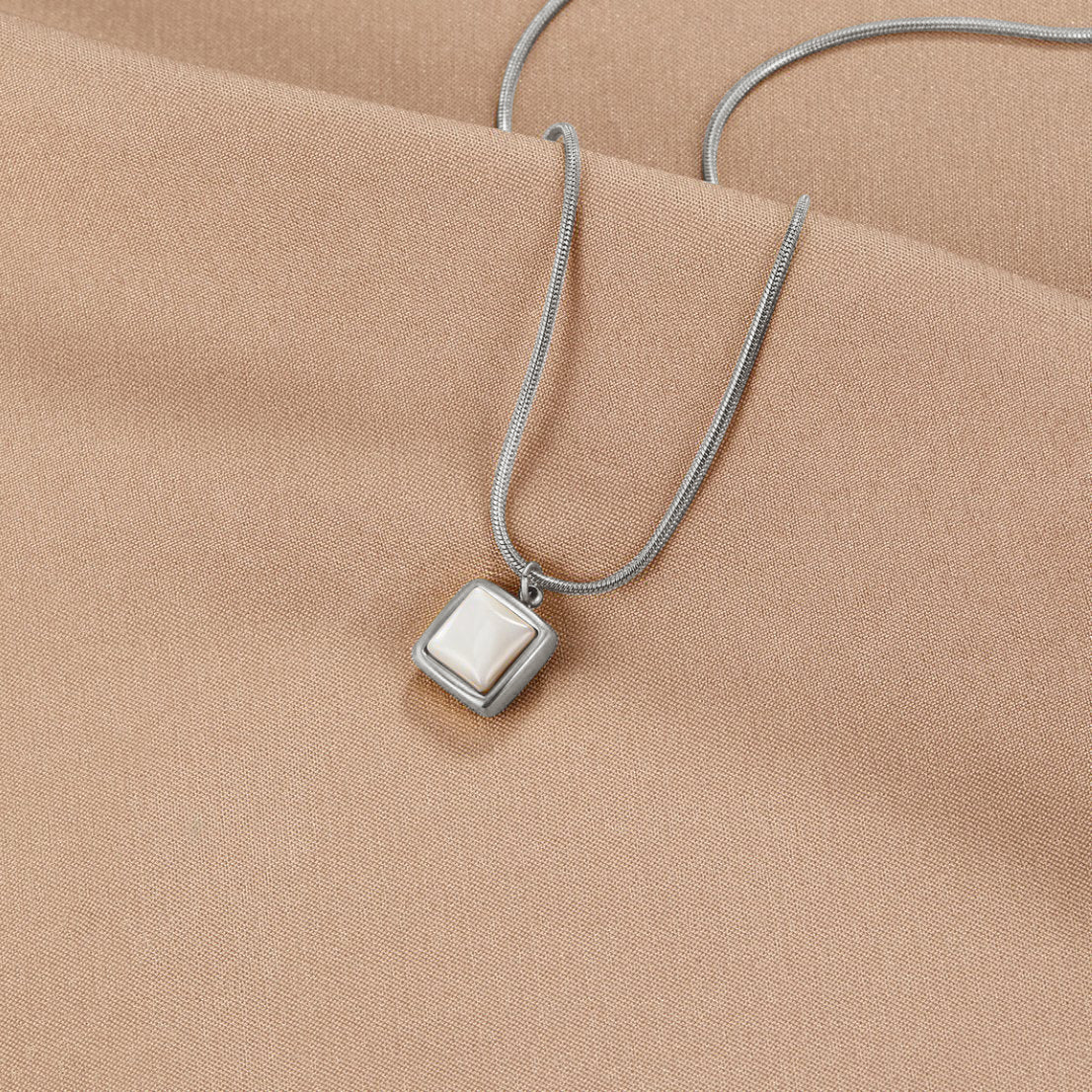 Riva Moonstone Pendant Necklace, lying on beige fabric, silver square pendant with cream stone