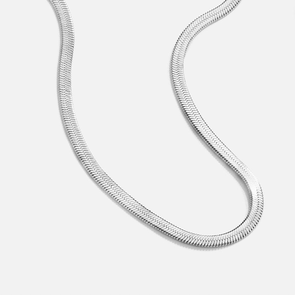 Sarya Snake Chain Silver Necklace, flat-lay close-up of a silver herringbone chain curving on