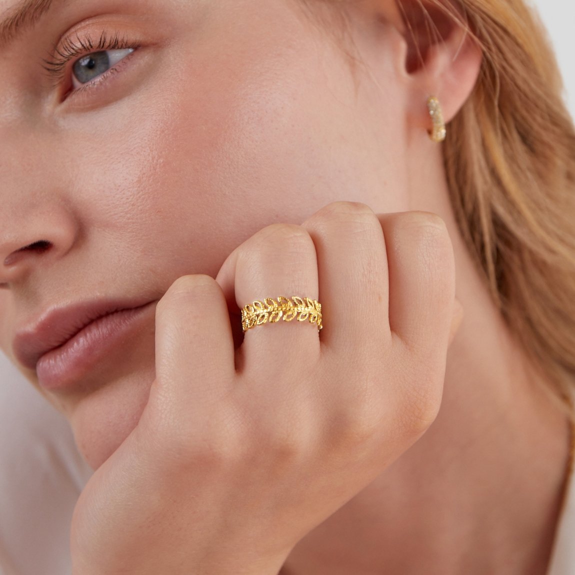 Summer Bloom Leaf Ring, worn on a hand against a cheek, with a gold hoop earring