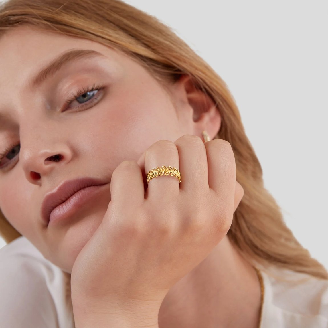 Summer Bloom Leaf Ring, worn on a hand resting against a cheek, gold leaf band