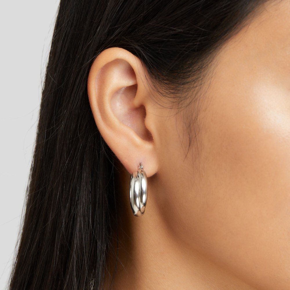Talia Silver Hoop Earrings, worn in an ear with dark hair pulled back, polished silver hoop