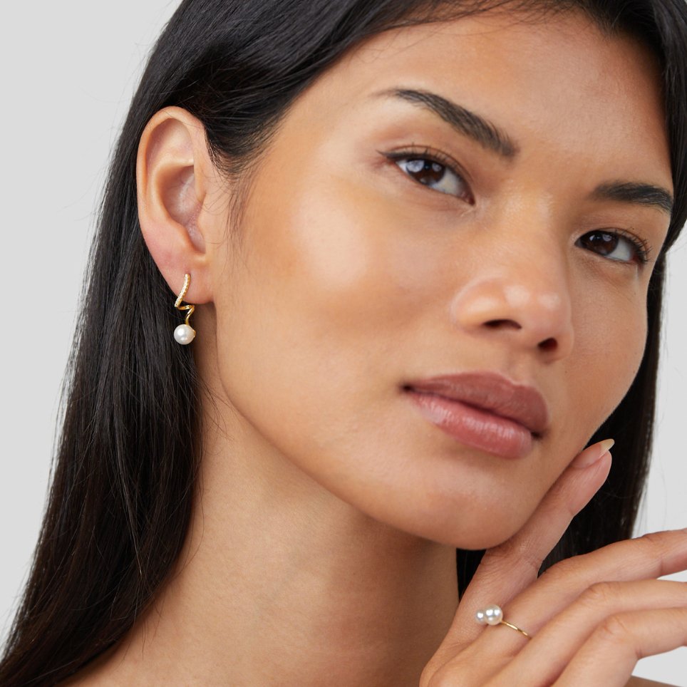 Tamara Pearl Wave Earrings, worn on an ear by a model, with a pearl ring on a hand