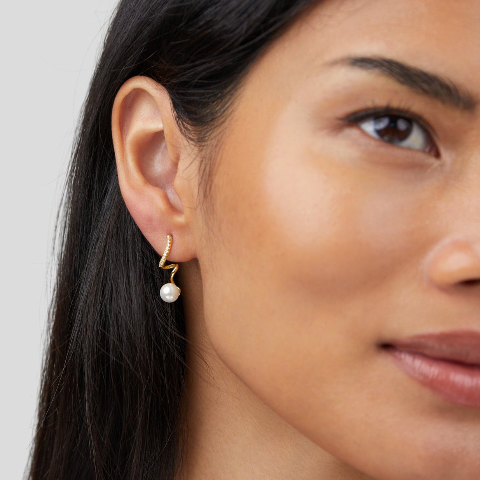 Tamara Pearl Wave Earrings, worn on an ear, gold hoop with a dangling pearl drop