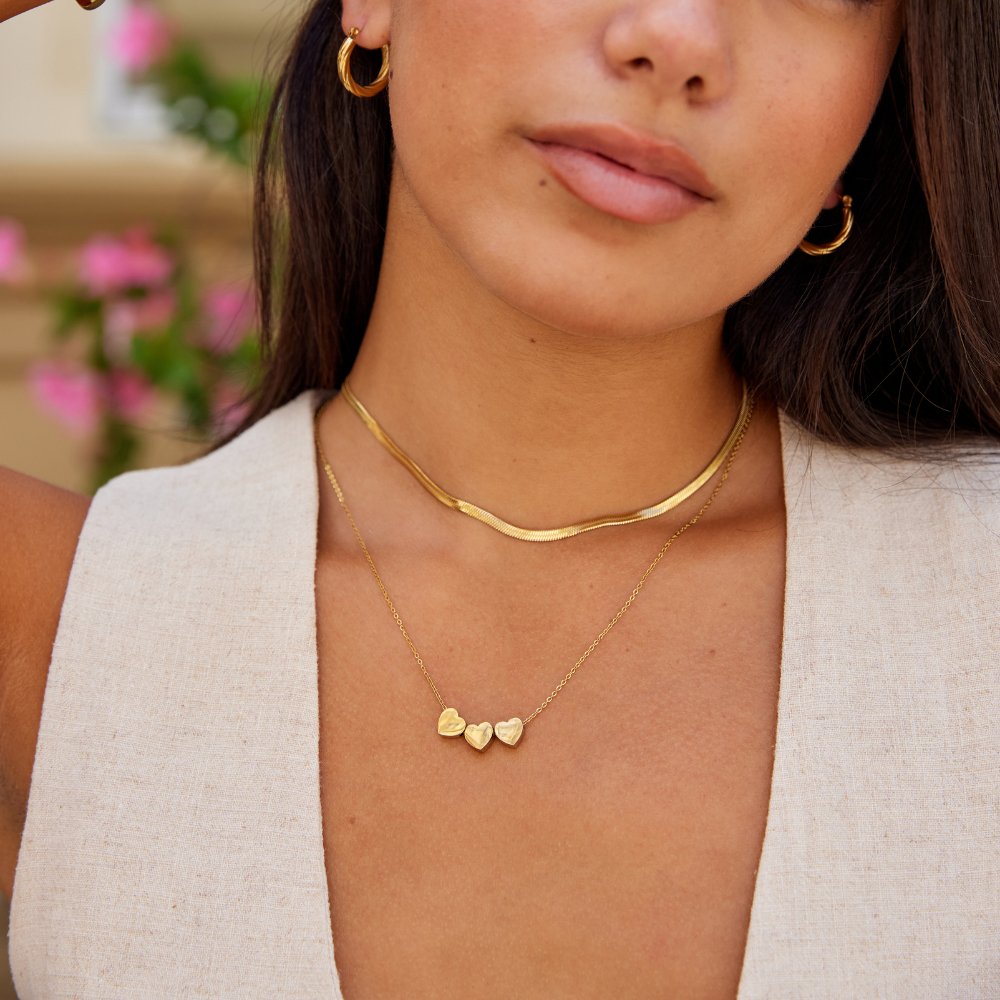 Trio Heart Pendant Necklace, worn on a neck with a gold herringbone chain and gold hoop earrings