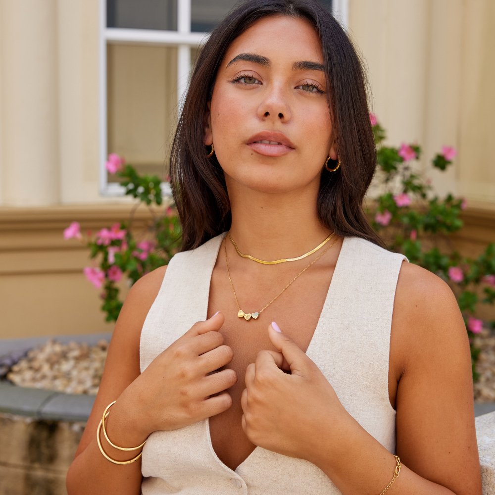Trio Heart Pendant Necklace, worn on a model with gold necklaces, hoops and bracelets