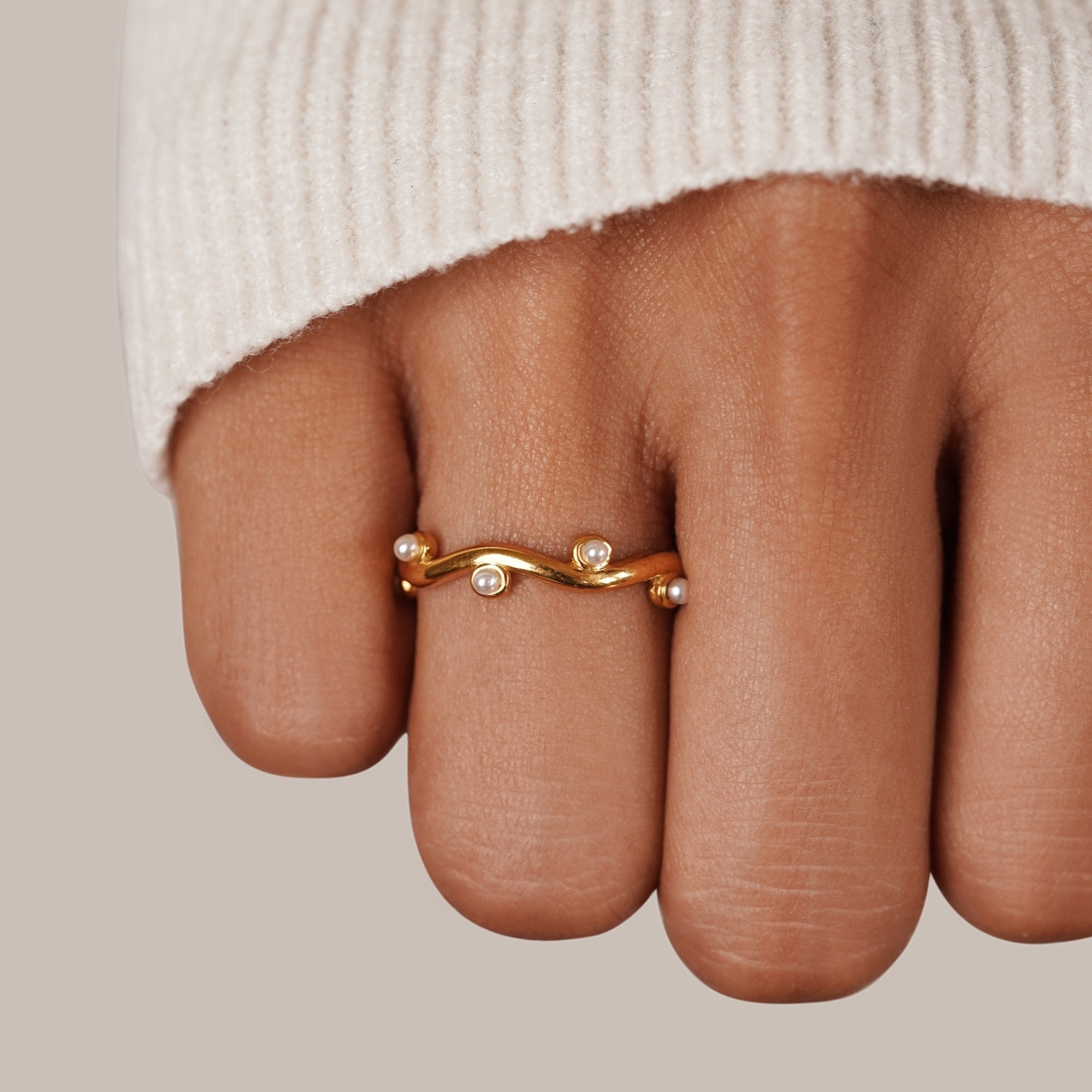 Wavey Pearl 18K Gold Ring, worn on a hand in a cream knit sleeve, wavy gold band with pearls
