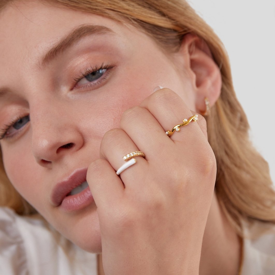 Wavey Pearl 18K Gold Ring, worn on a hand against a face, with gold rings and a white enamel ring