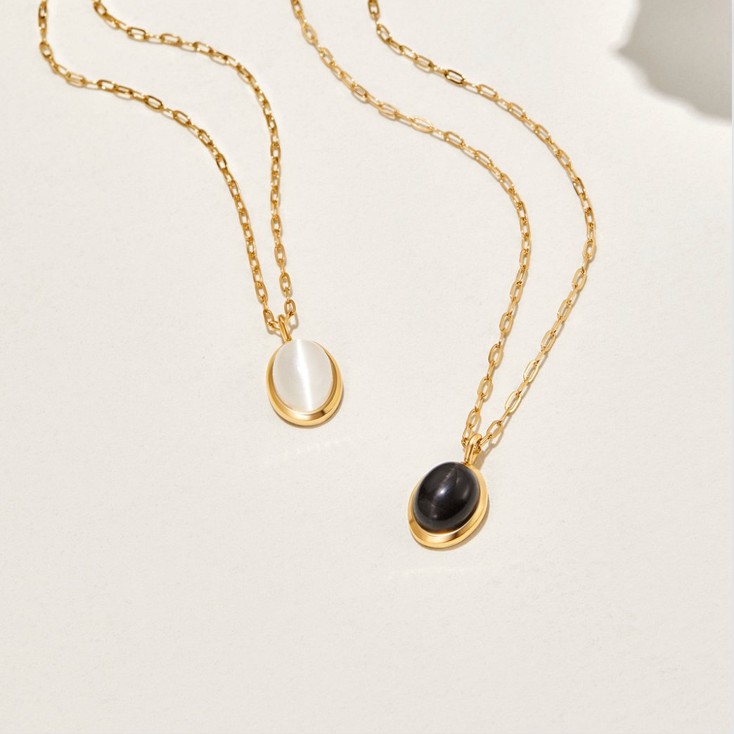 White Opal Necklace, two gold oval pendant necklaces laid flat, one white and one black stone